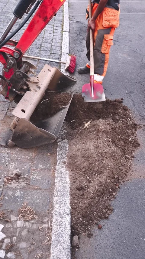 Worker with a shovel and a mini excavator at road works Stock Footage 314217060