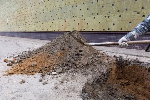 Worker with shovel is digging a pit on construction site. Concept of hard work Stock Photos