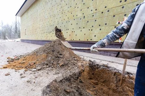 Worker with shovel is digging a pit on construction site. Concept of hard work Stock Photos