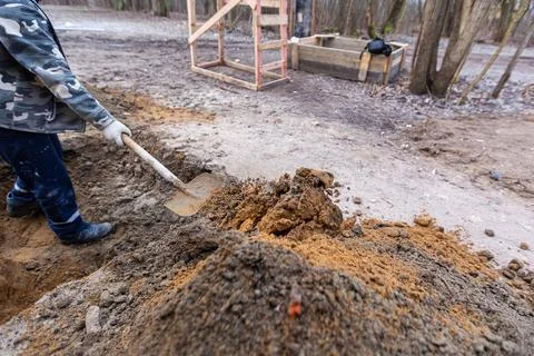 Worker with shovel is digging a pit on construction site. Concept of hard work Stock Photos