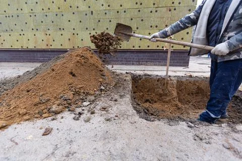 Worker with shovel is digging a pit on construction site. Concept of hard work Stock Photos