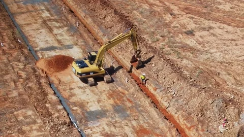 Worker with a shovel moving soil after track loader has dropped a load in trench Stock Footage 266479483