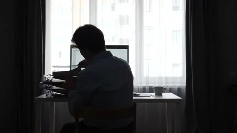 Worker silhouette sitting at a desk in front of a computer screen, holding a Stock Footage 346250805