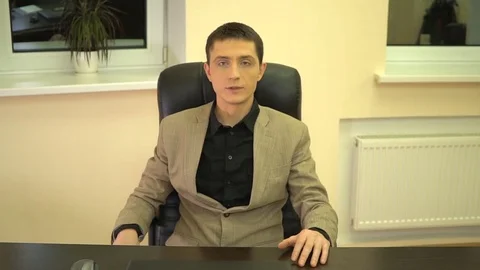 Worker sits in a chair and says looking at the camera and gesticulating with his Stock Footage