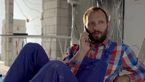 Worker sitting on the floor in his new flat and talking on cellphone, steadycam  Stock Footage 76502171
