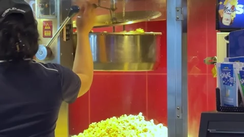 A worker skillfully manages a large popcorn machine at a bustling movie theater, Stock Footage 313910837