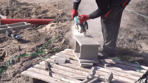 Worker slicing concrete block on site using angle grinder tool. Stock Footage 312880656