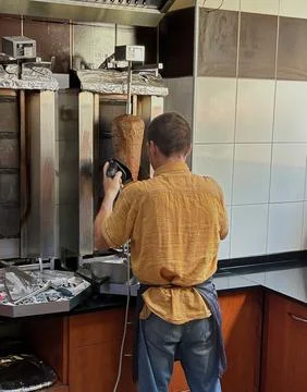 Worker slicing meat from a vertical kebab spit. Stock Photos
