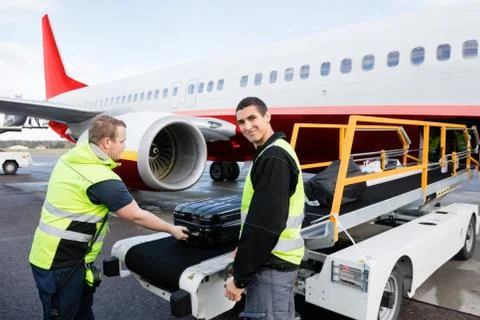 Worker Smiling While Colleague Unloading Luggage On Runway 스톡 사진