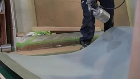 Worker spray painting a large flat board with grey green primer using a 動画素材 347123999