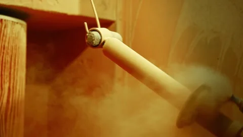 Worker spraying powder coating onto suspended cylindrical automotive component Stock Footage 338018427