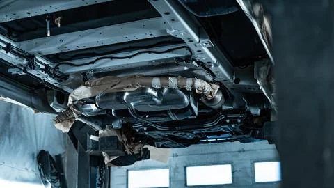 Worker Spraying Protective Undercoating Beneath a Car in Auto Workshop Stock Photos