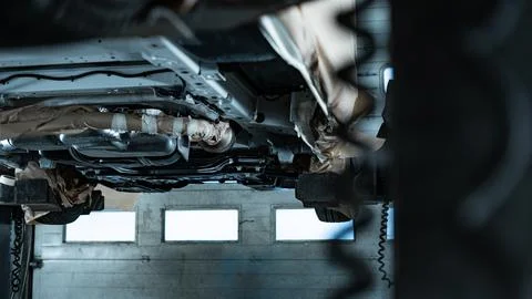 Worker Spraying Protective Undercoating Beneath a Car in Auto Workshop Foto stock