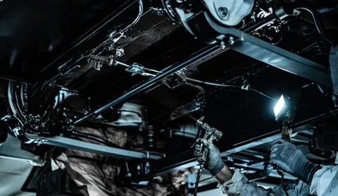 Worker Spraying Protective Undercoating Beneath a Car in Auto Workshop Stock Photos