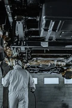 Worker Spraying Protective Undercoating Beneath a Car in Auto Workshop Stock Photos