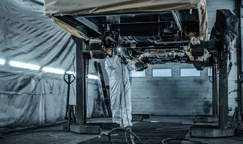 Worker Spraying Protective Undercoating Beneath a Car in Auto Workshop Stock Photos