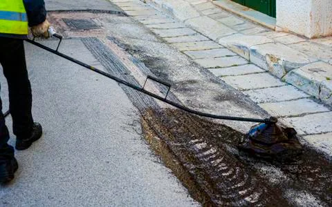 The worker sprays bitumen on the asphalt surface. Stock Photos