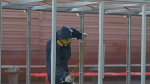 Worker sprays metal structure in industrial workshop during daytime production Stock Footage 310330737