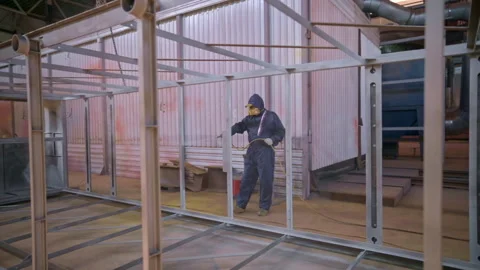 Worker sprays metal structure in industrial workshop during daytime production Stock Footage 310337088