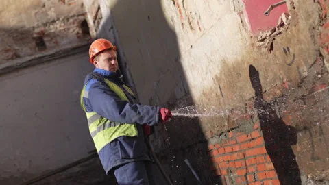 Worker sprays water on cement-smeared bricks with long hose Stock Footage 314648822