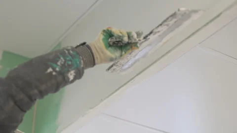 Worker spreads plaster across wall with wide trowel Stockbeeldmateriaal 314886731