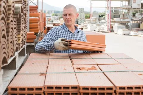 Worker stacking bricks in warehouse of materials Stockfoto's