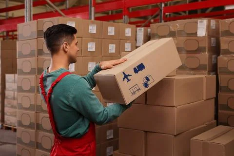Worker stacking cardboard boxes with shipping icons in warehouse. Wholesaling Stock Photos