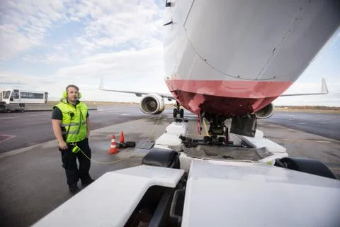 Worker Standing By Airplane With Communication Cable On Runway 写真素材