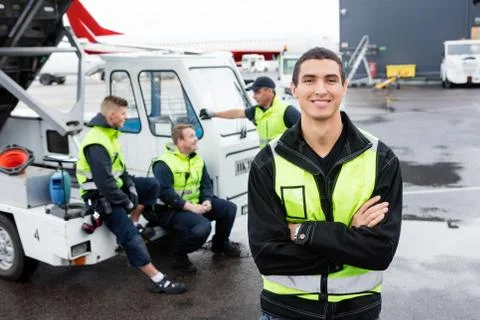 Worker Standing Arms Crossed While Colleagues Communicating At G Stock Photos