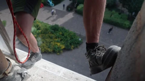 Worker standing on a high ledge with a safety rope overlooking a garden Stock Footage 301635873