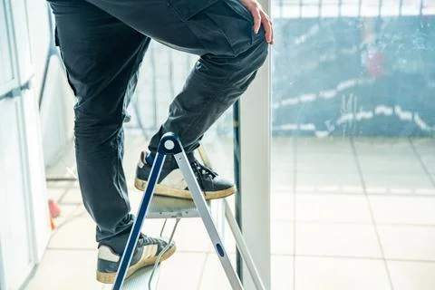 Worker standing on ladder during window repair or installation process at home Stock Photos