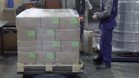 The worker is standing near the big cube of boxes being covered with film on the Stock Footage 84978607