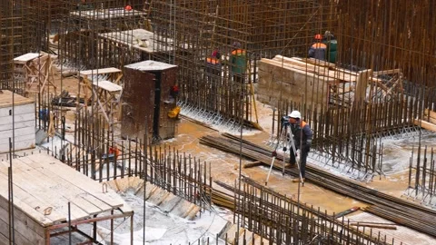 A worker stands on a construction site and looks through a rangefinder. Panorama Stock Footage 303410230