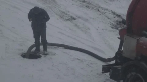A worker stands near a sewer hatch and a hose of a sewage pumping machine, slow Stock-Footage 314888579