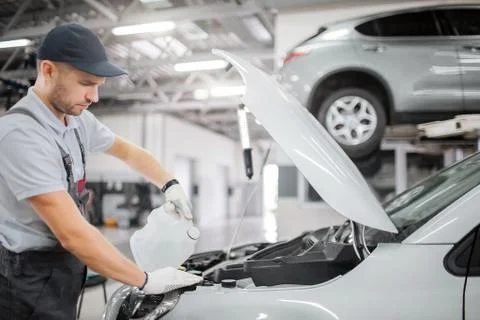 Worker stands at opened front body of car. He pours gasoline from canister. H Stock Photos