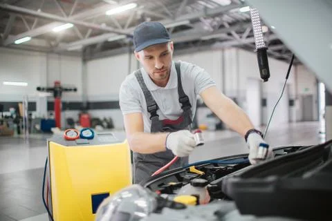 Worker stands at opened front part of car body. He holds power cords for conn Stock-Fotos