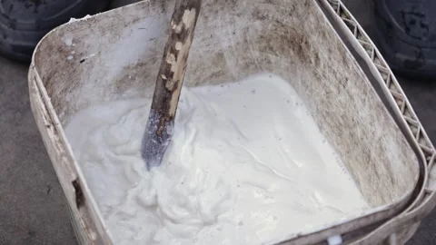 Worker stirring thick white paint with a wooden stick in a dirty plastic bu.. Vídeo Stock 337629889