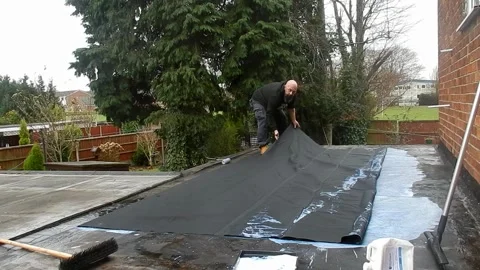 Worker stretching a rubber membrane over a painted waterproof layer on a flat Stock Footage 296573489