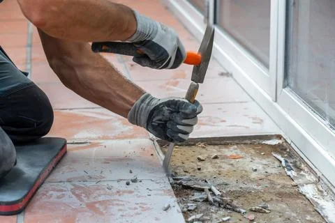 Worker strikes a chisel with a hammer to remove old ceramic tiles from the fl 写真素材