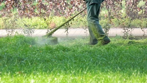 Worker with a string lawn trimmer mower cutting grass. 動画素材 90496669