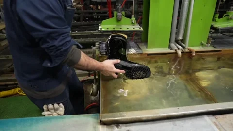 Worker submerging a glossy black rubber boot into a water tank to check for Stock Footage 342897191