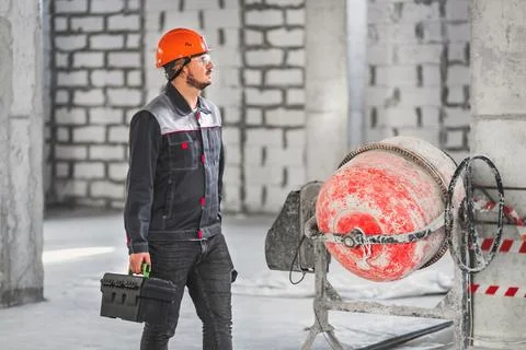 A worker with a suitcase with tools, in overalls, walks along a construction Stock Photos