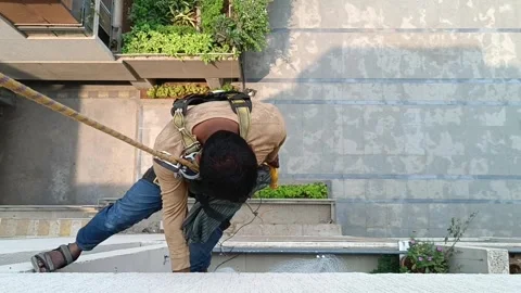 A worker suspended by a harness drills into a high-rise building for safety net Stock Footage 305453751