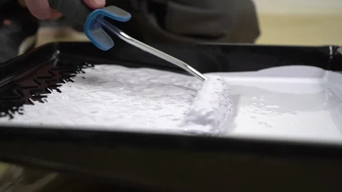 The worker takes white paint from the tray with a small roller. Stock Footage 125183889