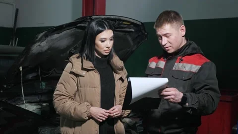 Worker talks to client showing cost list near broken car 库存影片 149470241