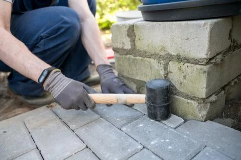 Worker tapping paving stones with rubber mallet Stock Photos
