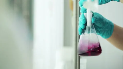Worker of the testing center at oil depot mixes the liquid in glass beaker, chan Stock Footage 199487258