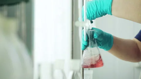 Worker of the testing center at oil depot mixes the liquid in glass beaker, chan Stock Footage 199487264
