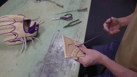 Worker threading purple lace through a baseball glove with a lacing needle at Stock Footage 340901434