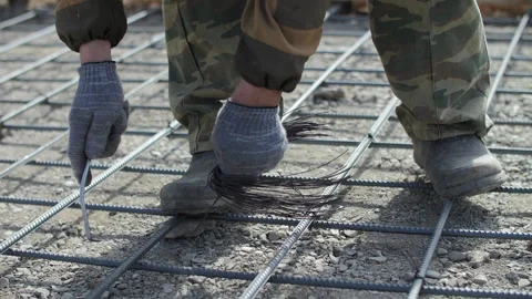 Worker ties reinforcement grid on concrete base Stock Footage 310406694